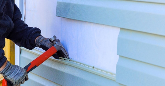 Worker removing the old siding of a house