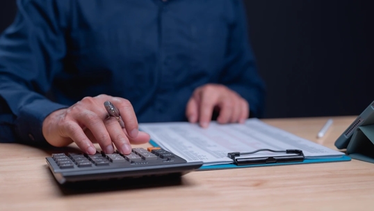 man using calculator with clipboard on desk