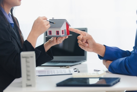 woman holding toy house over desk while man points at it