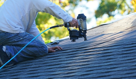 man nailing shingles to roof