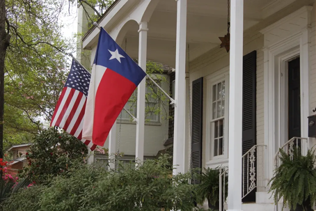 A classic white porch displays the Texas and US flags.