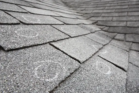 A close-up of an asphalt shingle roof with hail damage indicated by white chalk circles.