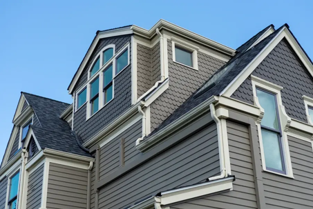 This is a low angle shot of a house with gray scalloped and horizontal siding.