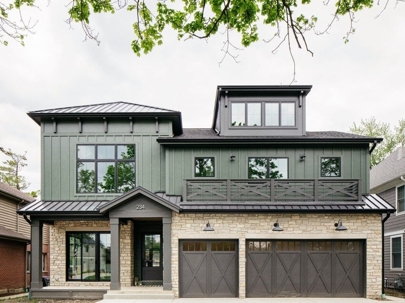 A modern green house with stone accents and a black trim.