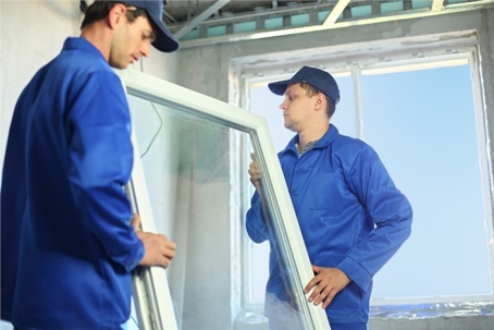 Two men in blue uniforms carefully lift a white-framed window