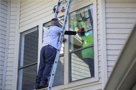 A man on a ladder washes a window. His shirt reads “Living You Love Excellence.”