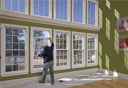 A man installs a replacement window in a bright, sunlit room with many windows.