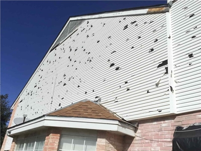 A close-up of a house with damaged white siding that appears to be worn from hail.