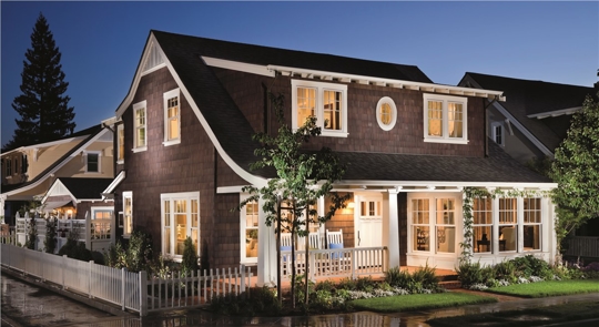 A two-story brown home at twilight with light pouring from the many windows.