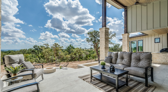 A covered patio with outdoor furniture sits on a large slab looking out over a treed landscape.