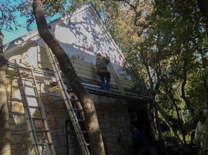 Workers are repairing a home's exterior siding with ladders