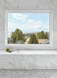 A picture of a window from an interior bathroom, showing a view of a city with trees, houses and a body of water.