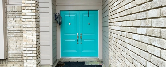 A turquoise double door is flanked by cream brick columns.