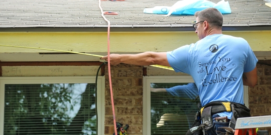 A worker measures the roofline with a tape measure.