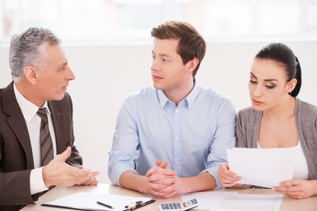 Three people meet at a table, discussing home renovations.