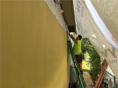 A worker stands on a ladder, securing siding to a home's exterior.