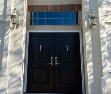 A straight on shot of a double door with silver hardware and knockers flanked by two lamps.
