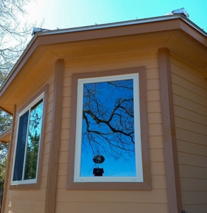 A photo of a building with two windows, the right one reflecting a tree and a blue sky.