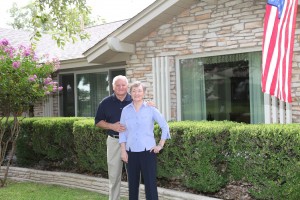 A photo of a senior couple standing in front of their home.