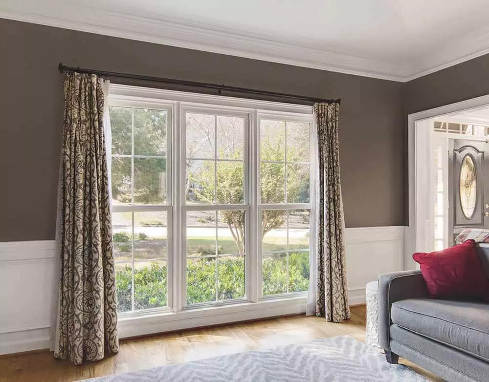 Three large white single-hung Infinity from Marvin windows in a bedroom with drapes open to either side of the windows. 
