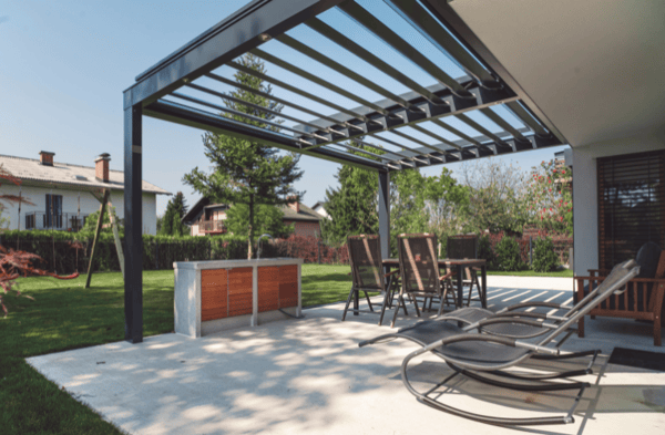 A gray gazebo with open slats over an outdoor patio with a furniture set in a backyard. 