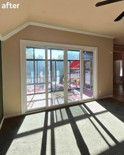 A white sliding patio door in place of the three windows in the same living room with light streaming through them.