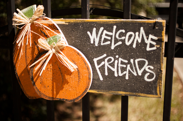 A rustic small wooden sign with orange pumpkins that reads "welcome friends" in a quirky font.