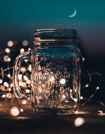 A mason jar with a handle in front of fairy lights laid out around the jar.