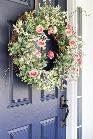 A blue door with a floral wreath with pink flowers hanging from it.