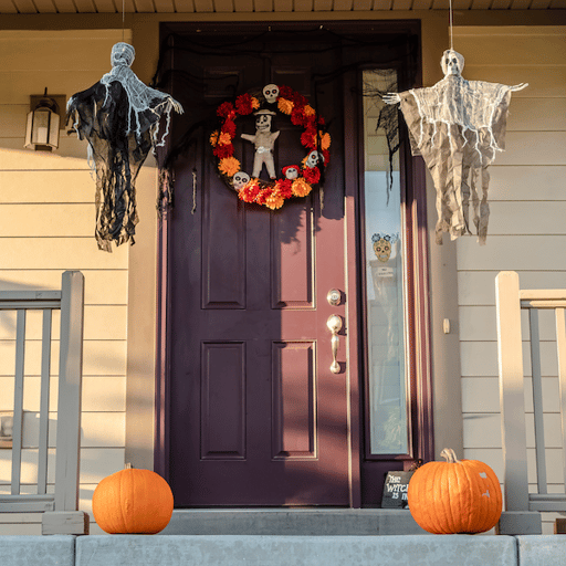 The front entryway of a home with pumpkins, hanging ghosts, and a voodoo doll wreath on the road.
