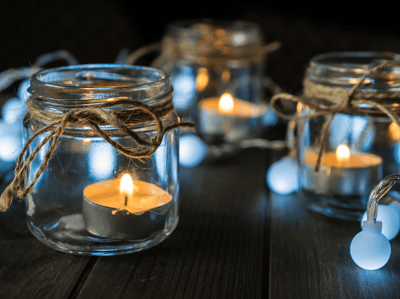 Small jars with twine tied around the top and small tea light candles lit inside the jars. 