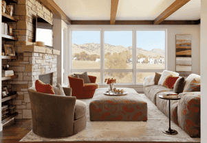 The inside of a living room with large windows on one wall, a fireplace and TV to the left, and a co…