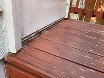 A close up of a wood deck with a red staining on it next to a white wall.