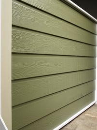 A warehouse wall of green dutch lap siding with space between the panels.