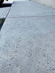A close up of a sidewalk with a rock salt concrete finish where there are small holes intentionally…