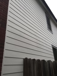 The side of a house with brick on the sides looking up with traditional horizontal lap siding.
