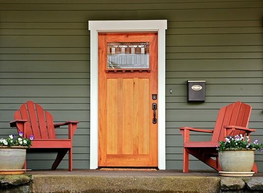 A photo of a house's front porch is shown with two red chairs, flowers, and a wood door in the cente…