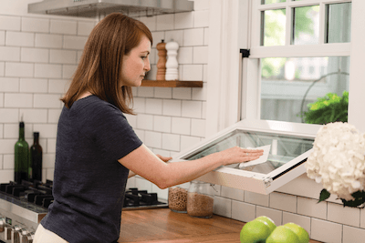 A woman with red hair and a navy shirt cleaning the outside of a single-hung window bottom sash in a…