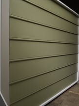 A siding sample in a warehouse of beaded seam siding that is army green.