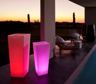 Illuminated planters around a pool at dusk. The planters are glowing red and pink.