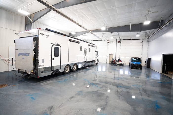 A blue and gray metallic epoxy coating in a large garage space with a white RV trailer and ATVs. 