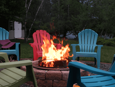 A fire pit with colored outdoor chairs circling it in a backyard.