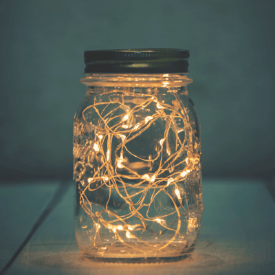 A mason jar with string lights glowing inside of it.