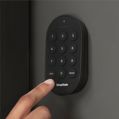 A black SimpliSafe door lock with a finger pressing one of the buttons. 