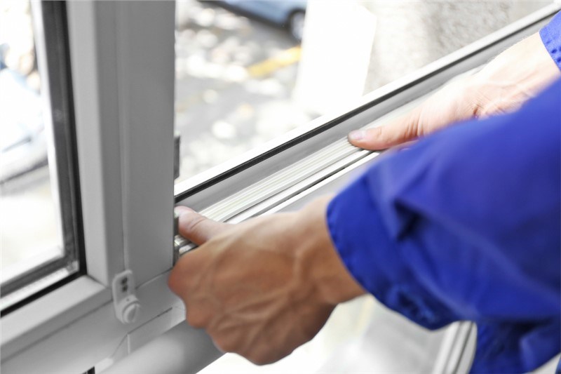 Two hands reaching to open a window sash. The arms have blue long sleeves on and the window is white.