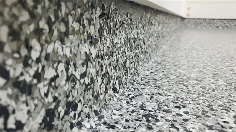 The intersection of a floor and wall with a coating that is made up of grey, white, and black flakes to give it a rock-like finish.