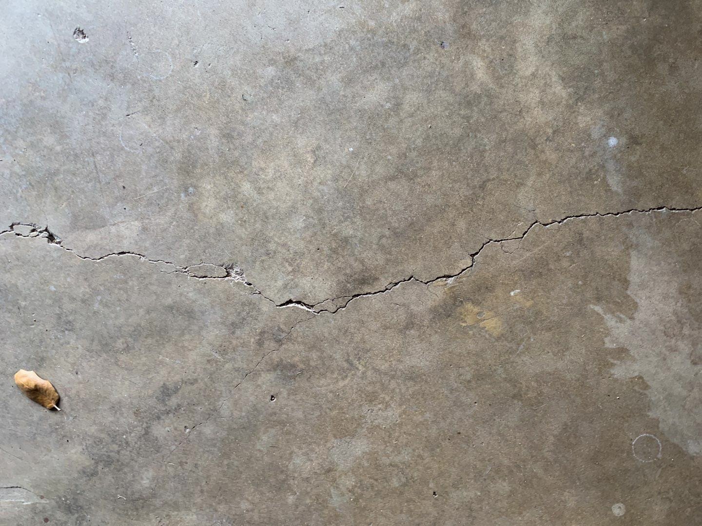 A close up of a bare concrete floor with a large crack going horizontally across.