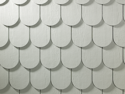 A close up of white scalloped shingle siding where the panels are rounded on the bottom and layered on top of each other.