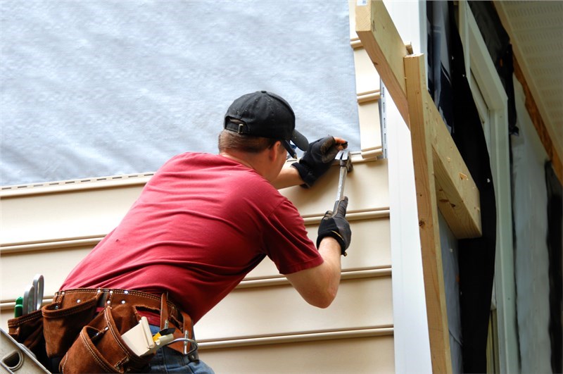A man hammering a nail into siding as he installs it on a home.