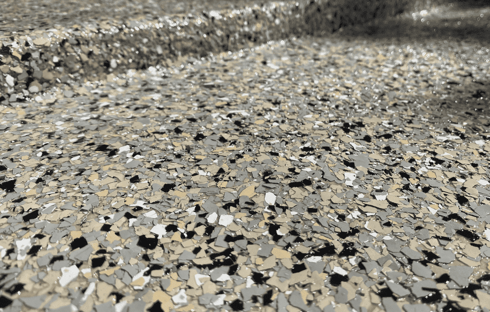 A close up of the lip of a garage with a concrete coating made of vinyl chips that are grey, white,…